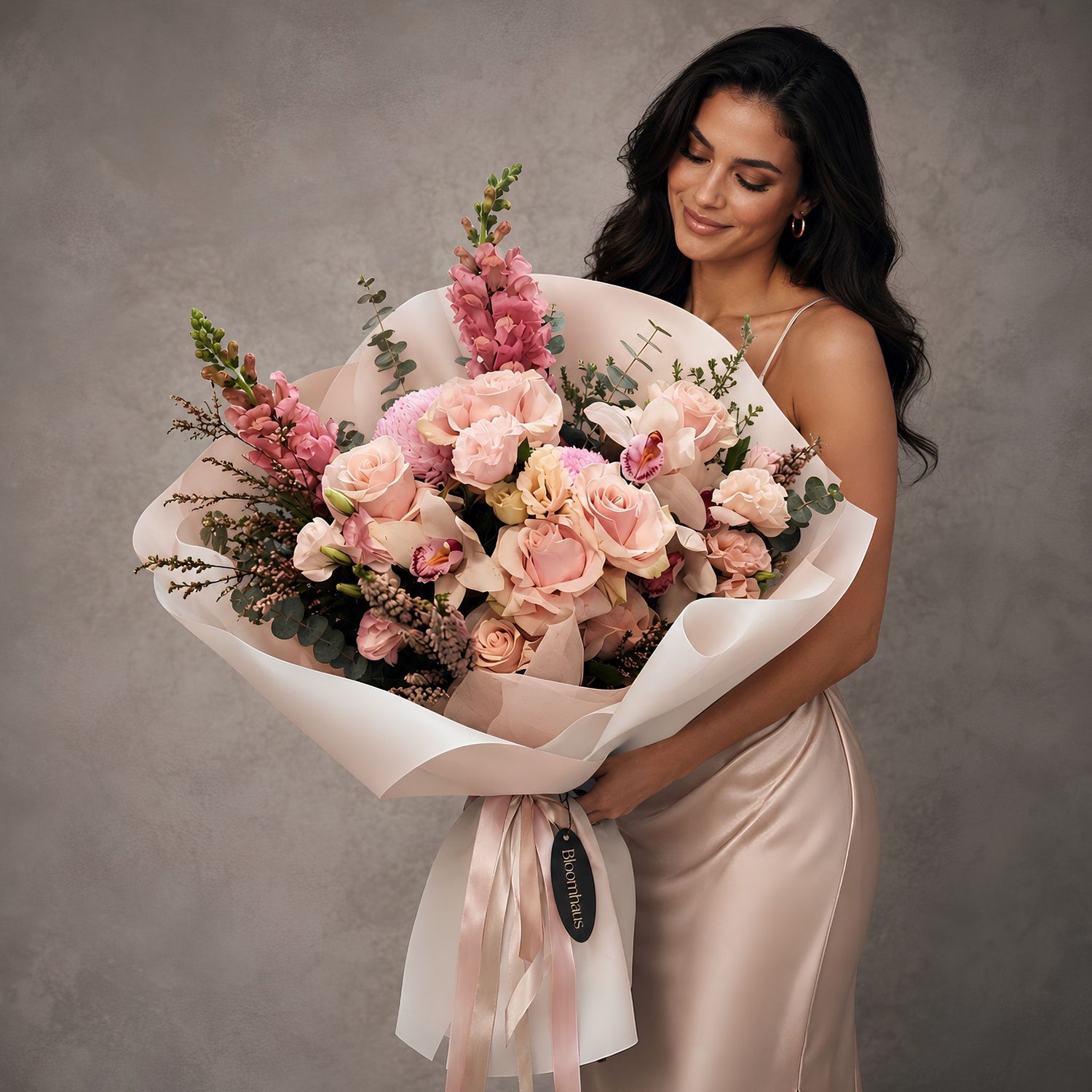 FLORAL PINK BOUQUET WITH GLAMOUROUS WOMAN HOLDING AGAINST A GREY WALL 