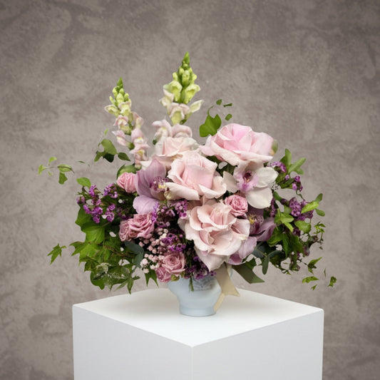 Pastel flower arrangement with roses in a ceramic pot by BLOOMHAUS MELBOURNE, featuring soft pink and purple blooms.