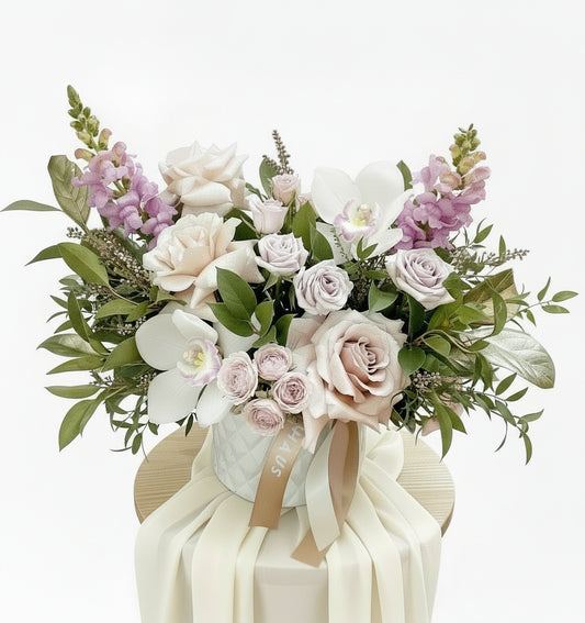 nude pink roses and lilac snap dragons with orchids in white ceramic pot on stand with cream chiffon and white background