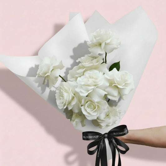 Bloomhaus Melbourne Bouquet of white Reflexed roses  wrapped in paper with a ribbon against a pink background